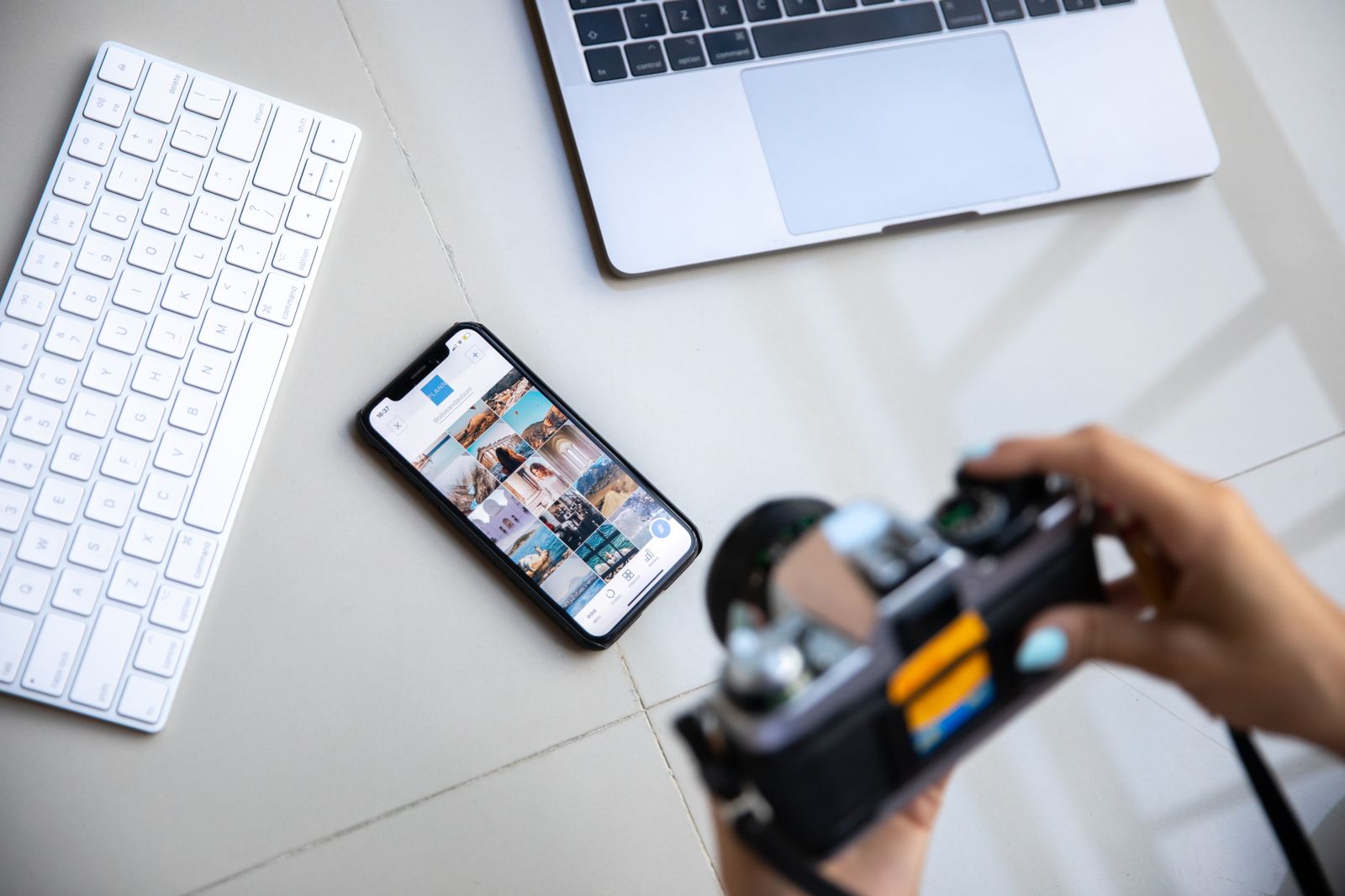A phone showing a social feed beside a laptop and camera